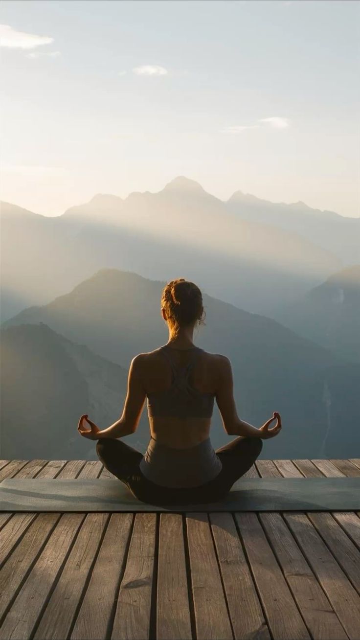 Woman meditating on a wooden deck overlooking misty mountains at sunrise