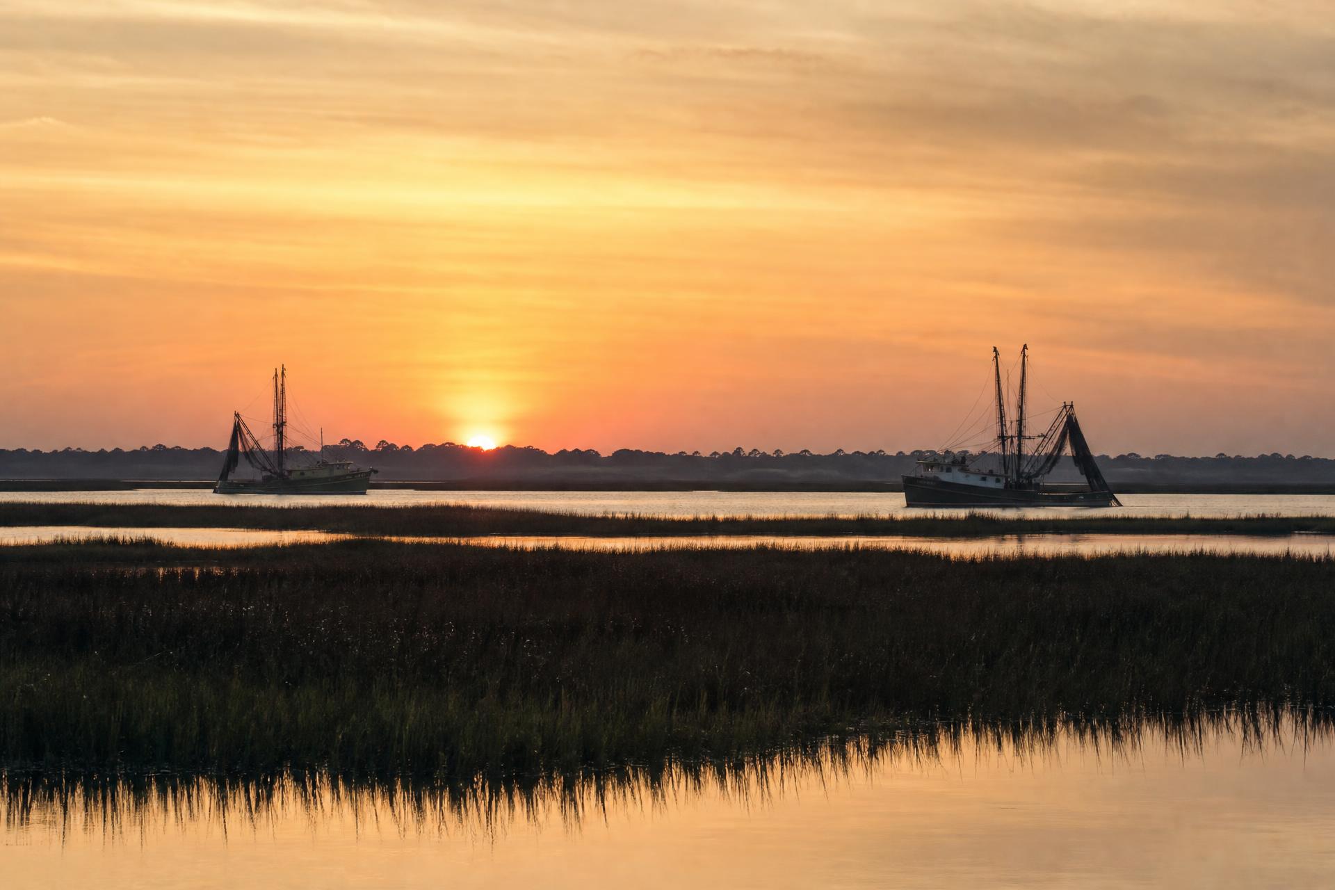 Lowcountry shrimp boats silhouetted against a fiery sunset